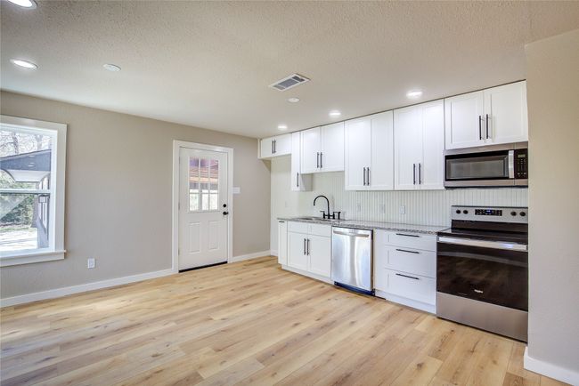 Kitchen with light stone counters, a sink, light wood-type flooring, appliances with stainless steel finishes, and white cabinetry | Image 10