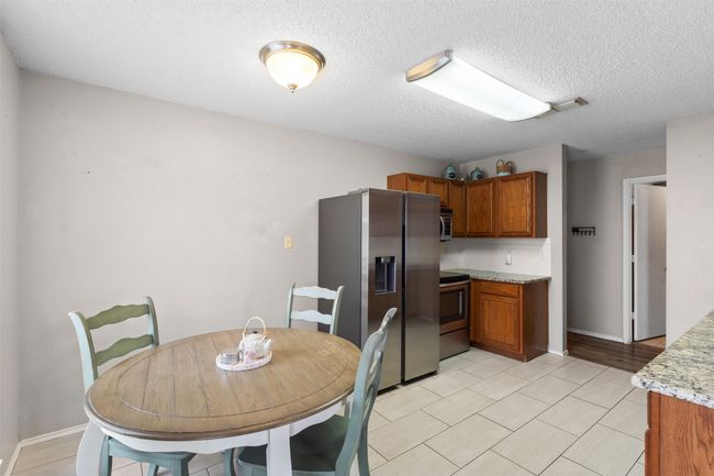 Kitchen featuring stainless steel appliances, brown cabinets, a textured ceiling, light tile patterned floors, and baseboards | Image 12