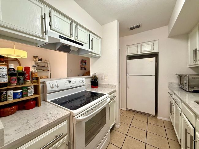 Kitchen featuring visible vents, under cabinet range hood, a toaster, light tile patterned flooring, and white appliances | Image 6