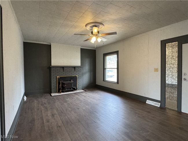 Unfurnished living room featuring a wood stove, ornamental molding, dark hardwood / wood-style floors, ceiling fan, and brick wall | Image 7