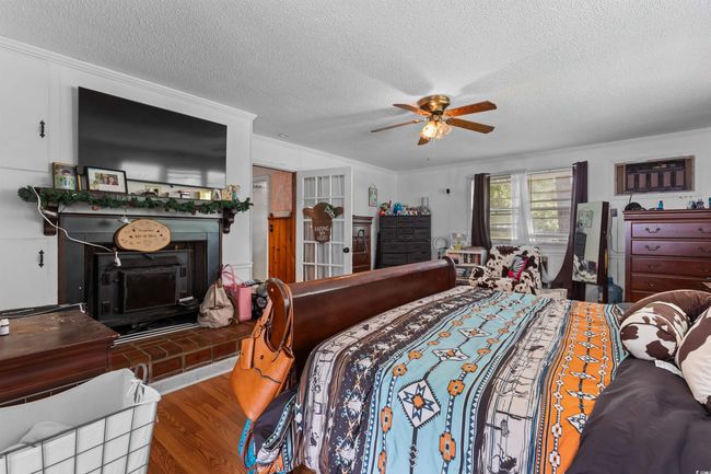 Bedroom with a textured ceiling, wood finished floors, a fireplace, ceiling fan, and crown molding | Image 24