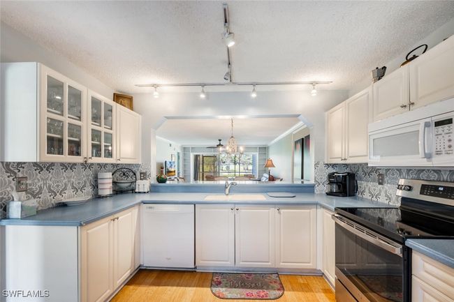 Kitchen featuring light wood-style flooring, a sink, glass insert cabinets, and white appliances | Image 7