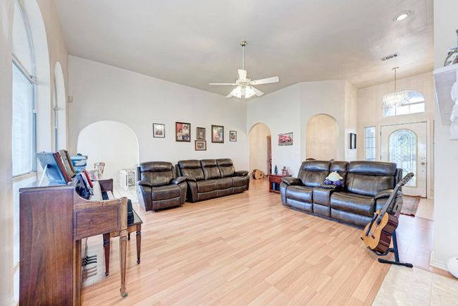 Living area with arched walkways, light wood finished floors, a chandelier, a ceiling fan, and recessed lighting | Image 13