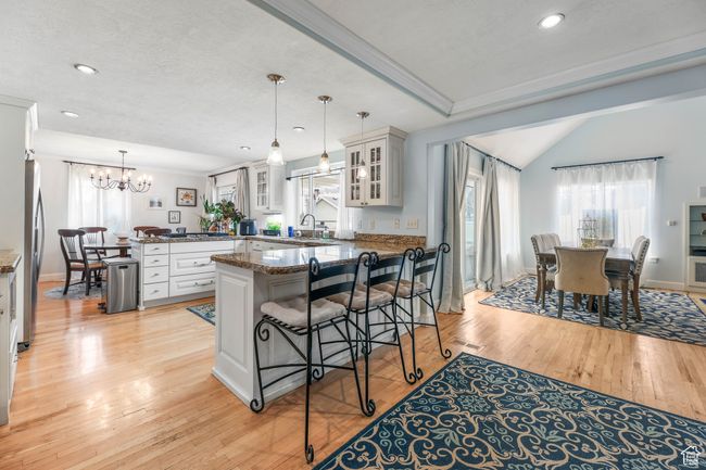 Kitchen with pendant lighting, crown molding, light wood finished floors, glass insert cabinets, and a peninsula | Image 8