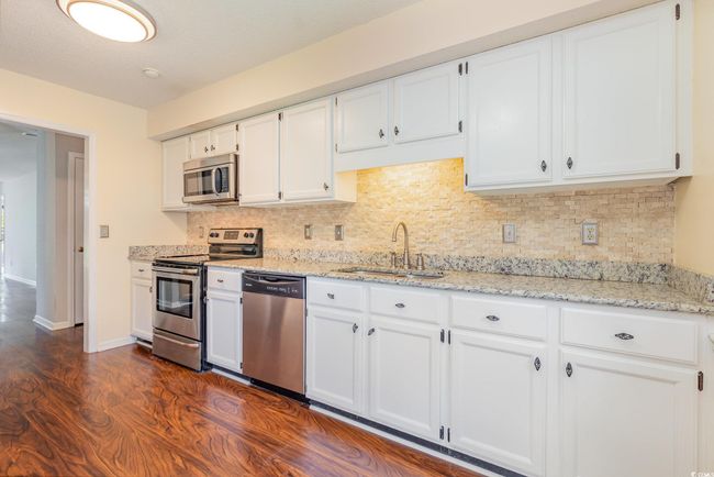 Kitchen with white cabinets, a sink, decorative backsplash, appliances with stainless steel finishes, and dark wood-style flooring | Image 14