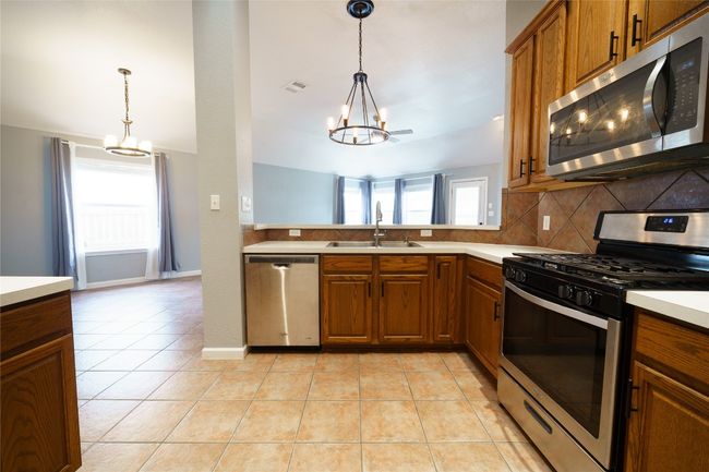 Kitchen featuring appliances with stainless steel finishes, a chandelier, a sink, brown cabinets, and decorative backsplash | Image 13