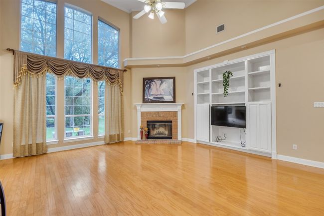 Unfurnished living room with ceiling fan, a high ceiling, wood finished floors, a brick fireplace, and crown molding | Image 12