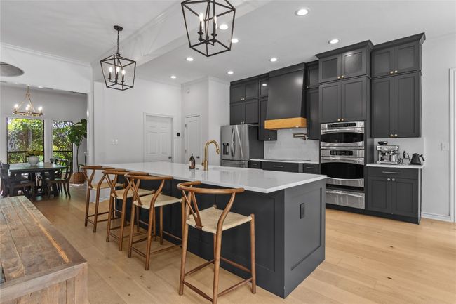 Kitchen featuring stainless steel appliances, an inviting chandelier, light countertops, a warming drawer, and custom range hood | Image 17