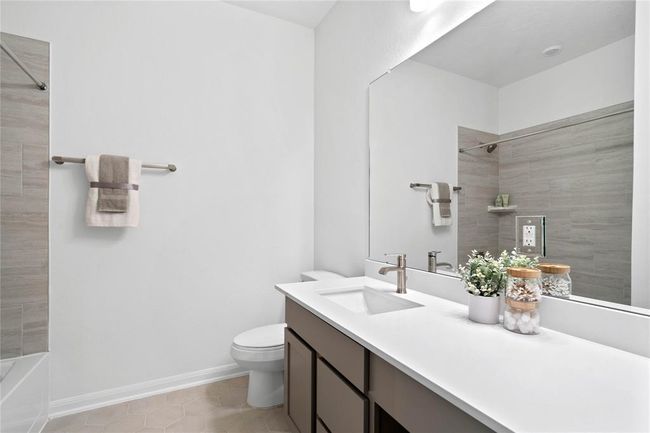 Secondary bath features tile flooring, bath/shower combo with tile surround, stained wood cabinets, beautiful light countertops, mirror, sleek fixtures and modern finishes. | Image 6