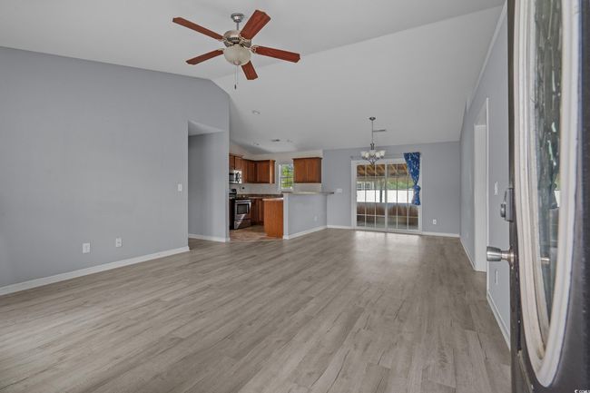 Unfurnished living room with lofted ceiling, a chandelier, a ceiling fan, light wood finished floors, and baseboards | Image 10