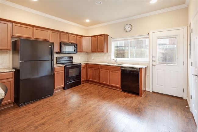 Kitchen featuring backsplash, wood finished floors, brown cabinets, and black appliances | Image 4