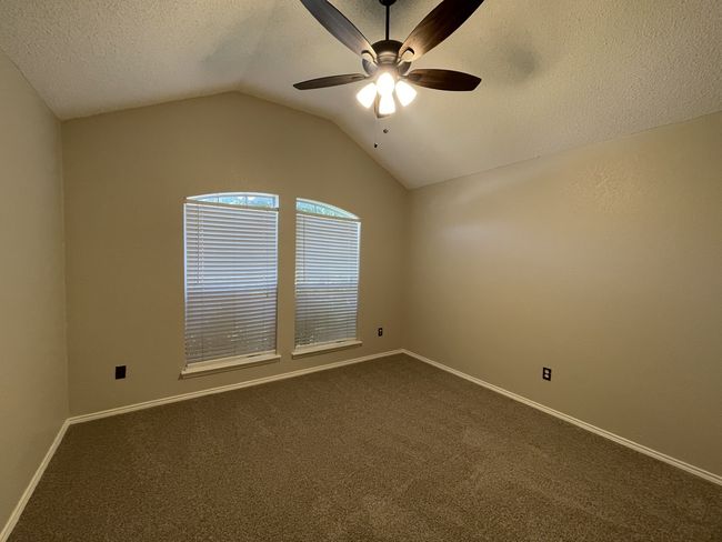 Empty room with vaulted ceiling, a ceiling fan, dark carpet, and a textured ceiling | Image 9