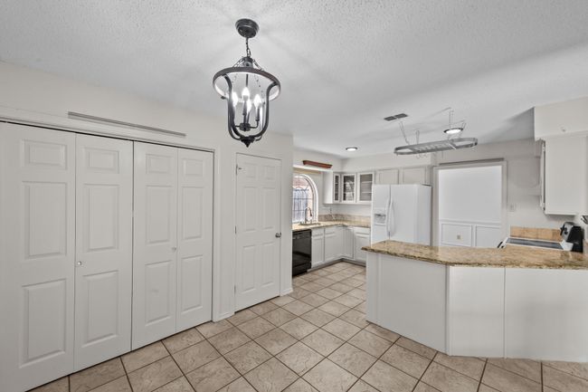 Kitchen with white appliances, a peninsula, a chandelier, glass insert cabinets, and white cabinets | Image 16