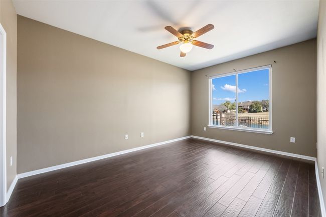 Primary bedroom with ceiling fan, wood flooring, and views of the back yard. | Image 16