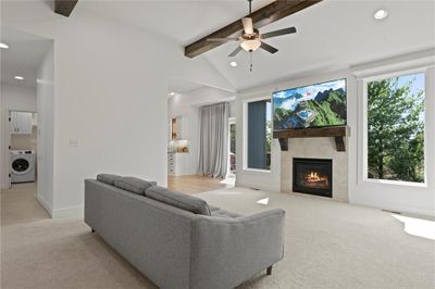 Carpeted living room with ceiling fan, a fireplace, vaulted ceiling with beams, and a healthy amount of sunlight | Image 3