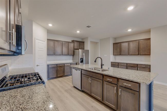 Kitchen with an island with sink, decorative backsplash, stainless steel appliances, a sink, and light wood-type flooring | Image 13