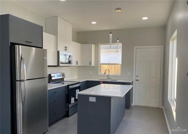 Kitchen with a center island, sink, hanging light fixtures, appliances with stainless steel finishes, and white cabinetry | Image 10