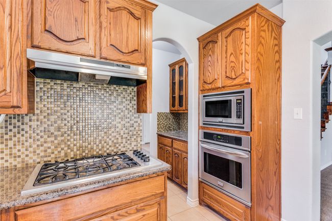 Kitchen with appliances with stainless steel finishes, extractor fan, tasteful backsplash, brown cabinets, and light tile patterned floors | Image 14