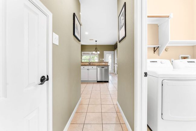 Laundry room featuring light tile patterned flooring, baseboards, washing machine and clothes dryer, and a chandelier | Image 31