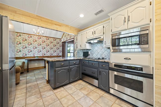 Kitchen with a peninsula, under cabinet range hood, visible vents, appliances with stainless steel finishes, and stone finish flooring | Image 11
