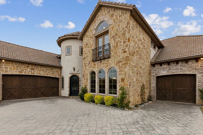 View of front of home featuring an attached garage, a balcony, stone siding, and decorative driveway | Image 36