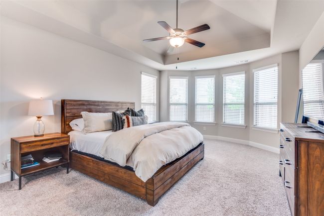Bedroom featuring a raised ceiling, light colored carpet, multiple windows, and baseboards | Image 17