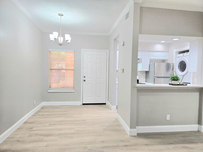 Entryway featuring stacked washer / drying machine, crown molding, a chandelier, light wood finished floors, and baseboards | Image 8