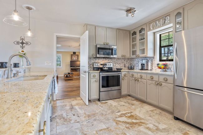 Kitchen featuring appliances with stainless steel finishes, a sink, decorative backsplash, glass insert cabinets, and hanging light fixtures | Image 18
