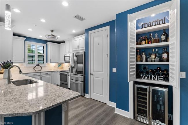 Kitchen with beverage cooler, appliances with stainless steel finishes, wood finished floors, white cabinets, and recessed lighting | Image 7