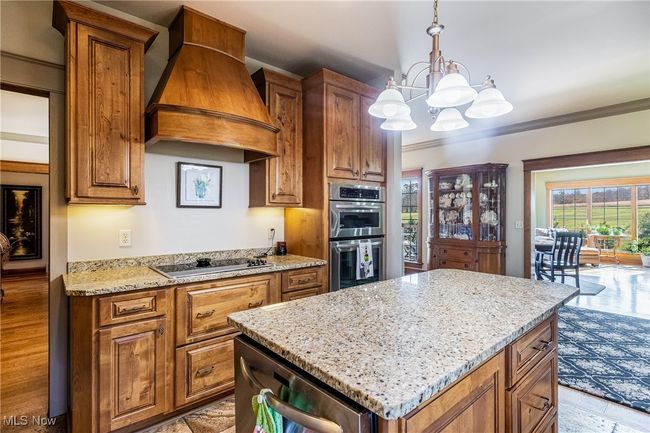 Kitchen featuring a center island, custom exhaust hood, black electric cooktop, crown molding, and wall oven | Image 17