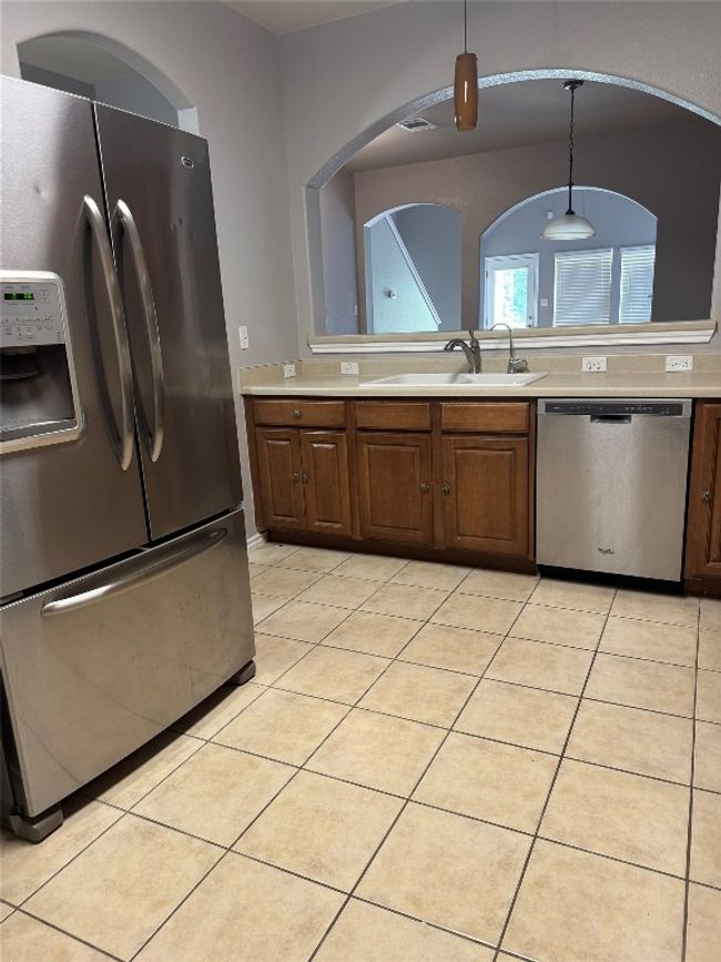 Kitchen with stainless steel appliances, light countertops, a sink, decorative light fixtures, and light tile patterned floors | Image 5