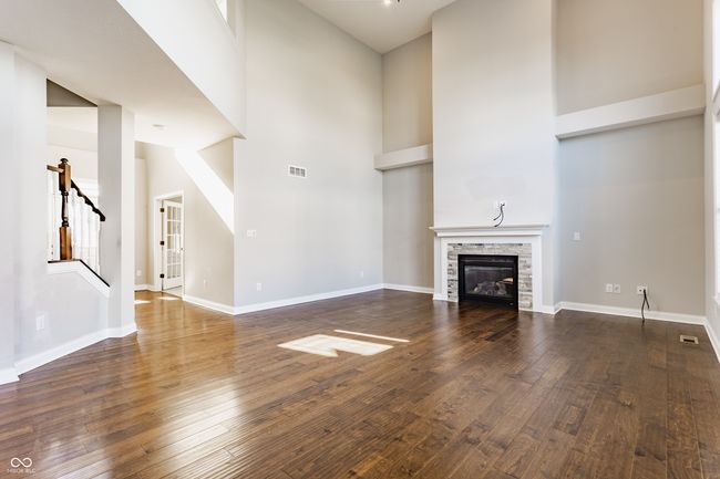 unfurnished living room with stairway, hardwood / wood-style floors, a high ceiling, visible vents, and a fireplace | Image 14