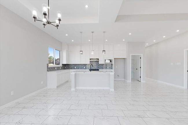 Kitchen featuring a chandelier, white cabinets, recessed lighting, light marble finish floors, and a kitchen island with sink | Image 15
