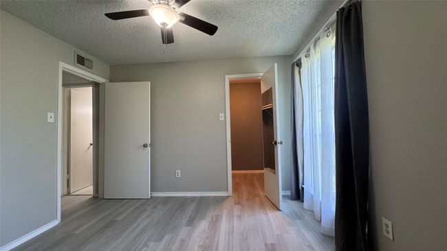 Unfurnished bedroom with a textured ceiling, light wood-style flooring, a spacious closet, a ceiling fan, and baseboards | Image 12