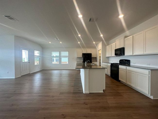 Kitchen with black appliances, open floor plan, an island with sink, dark wood-style floors, and white cabinets | Image 14