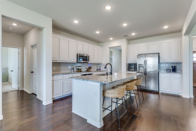 Kitchen with stainless steel appliances, decorative backsplash, a kitchen breakfast bar, white cabinets, and light stone countertops | Image 7