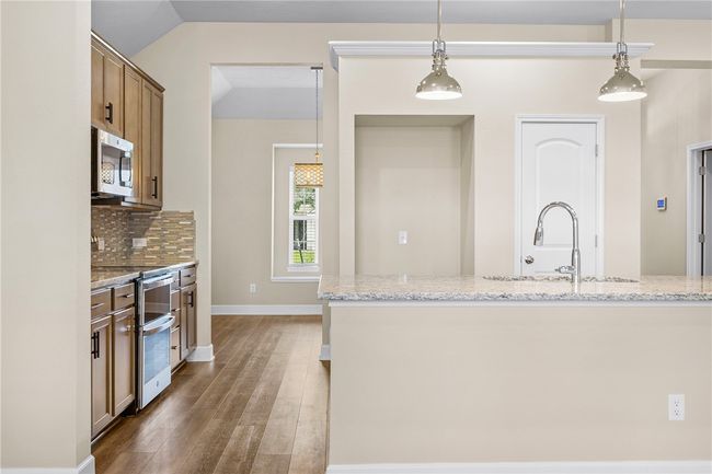 Kitchen with stainless steel appliances, wood finished floors, pendant lighting, light stone countertops, and lofted ceiling | Image 16