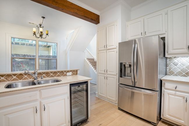 Kitchen featuring tasteful backsplash, stainless steel refrigerator with ice dispenser, wine cooler, light wood finished floors, and a sink | Image 7