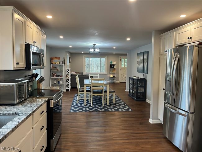 Kitchen with dark hardwood / wood-style flooring, stainless steel appliances, white cabinets, and light stone counters | Image 13