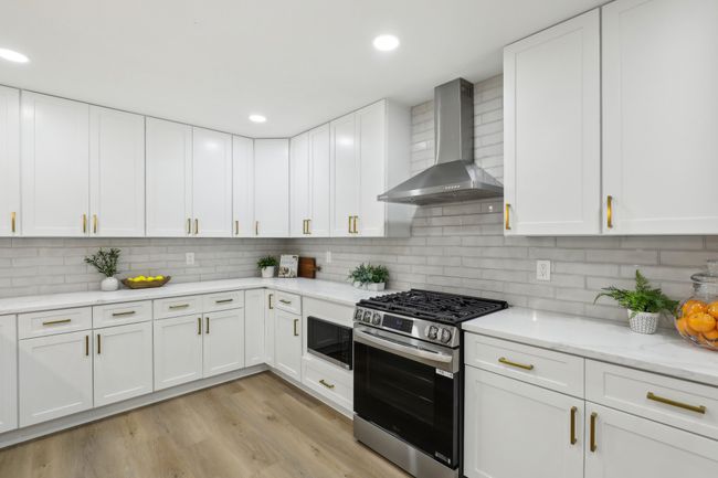 Kitchen featuring white cabinets, light wood finished floors, stainless steel appliances, wall chimney range hood, and backsplash | Image 8