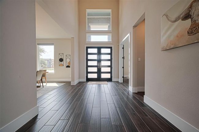 This photo showcases a spacious and bright entryway with dark wood Tile flooring, modern double doors, and high ceilings. Large windows bring in natural light, and adjacent rooms are visible, adding to the open feel. | Image 5