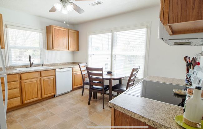 Kitchen featuring white dishwasher, a sink, a ceiling fan, light countertops, and exhaust hood | Image 4