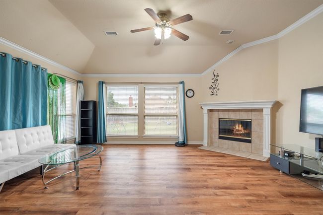 Living room featuring vaulted ceiling, ceiling fan, wood finished floors, a fireplace, and crown molding | Image 20