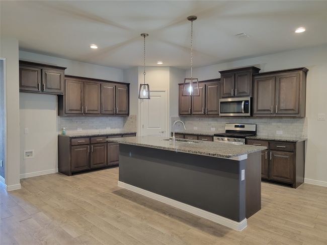 Kitchen featuring stainless steel appliances, a sink, dark brown cabinetry, light wood finished floors, and recessed lighting | Image 10