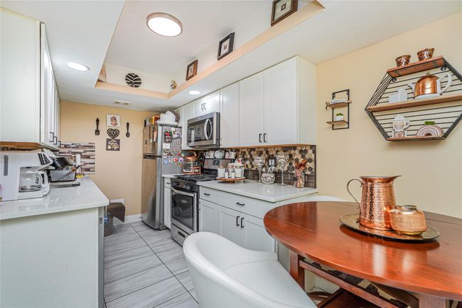 Kitchen featuring backsplash, white cabinetry, stainless steel appliances, and light countertops | Image 7
