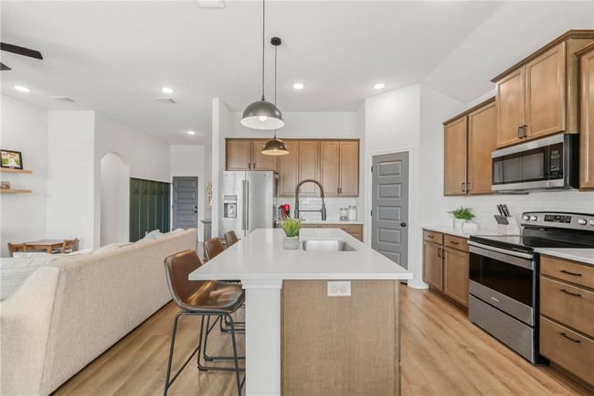 Kitchen featuring stainless steel appliances, open floor plan, light wood-type flooring, brown cabinets, and a breakfast bar | Image 15