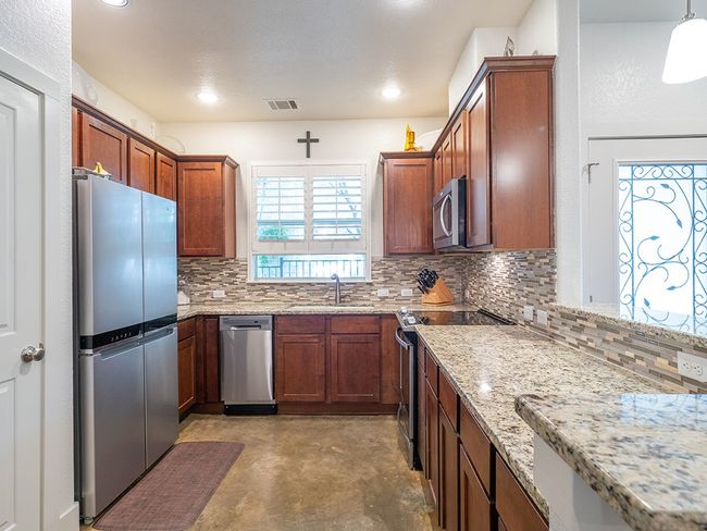 Kitchen with light stone counters, appliances with stainless steel finishes, finished concrete flooring, tasteful backsplash, and decorative light fixtures | Image 7