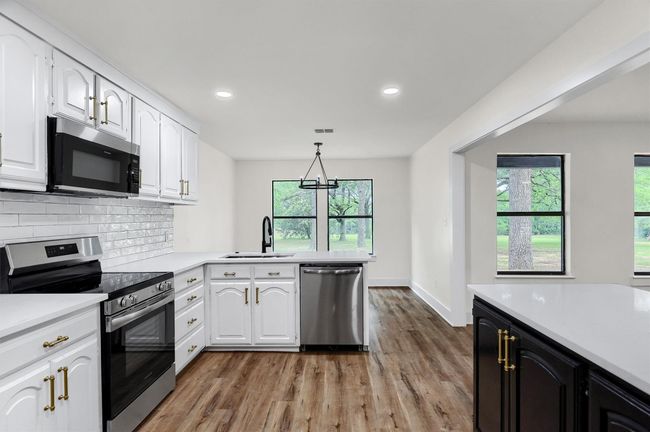 Kitchen featuring appliances with stainless steel finishes, a sink, light wood-style floors, light countertops, and white cabinetry | Image 11
