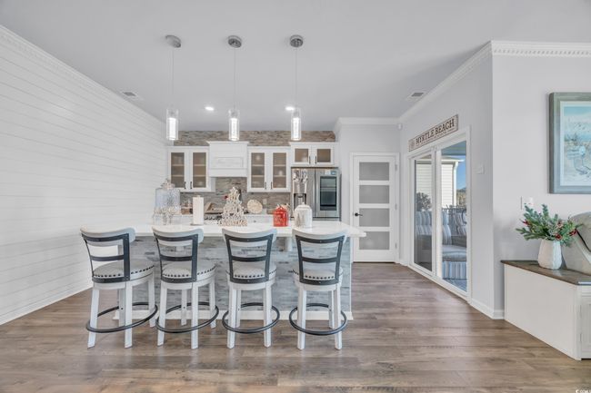 Kitchen featuring stainless steel fridge with ice dispenser, a kitchen bar, white cabinetry, glass insert cabinets, and decorative light fixtures | Image 15