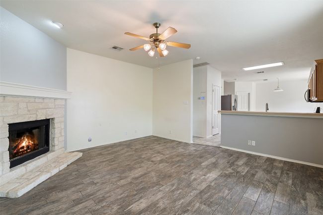 Unfurnished living room with visible vents, wood finished floors, a fireplace, baseboards, and ceiling fan | Image 21